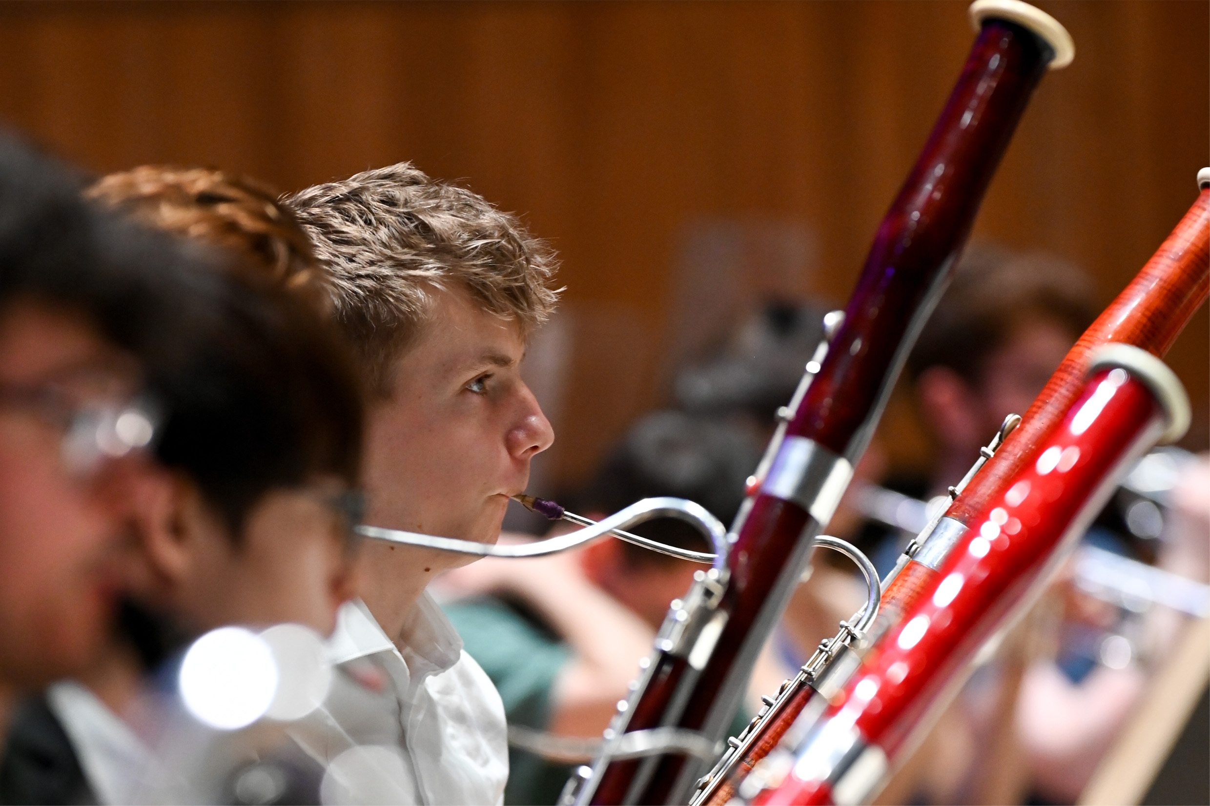 A group of bassoon students performing in an orchestral rehearsal, with a woo background panel.